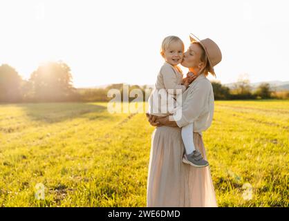 Schwangere Mutter küsst Tochter auf dem Feld bei Sonnenuntergang Stockfoto