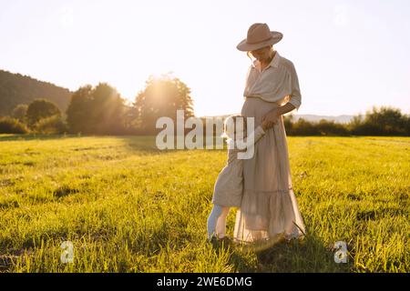 Schwangere Mutter, die bei Sonnenuntergang die Hand der Tochter auf dem Feld hält Stockfoto