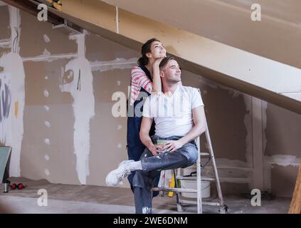 Lächelnder Mann, der auf einer Leiter sitzt und die Frau zu Hause steht Stockfoto