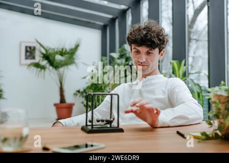 Lächelnder Geschäftsmann, der mit newtons Wiege im Büro spielt Stockfoto