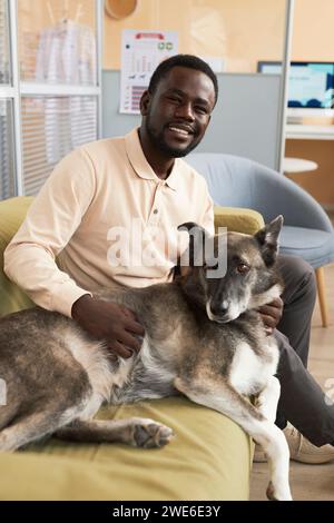 Glücklicher junger Mann, der mit Hund auf Sofa in der Klinik sitzt Stockfoto