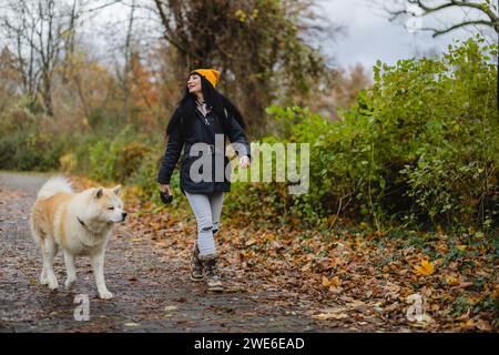 Lächelnde Frau, die mit Hund auf dem Fußweg im Herbstpark läuft Stockfoto