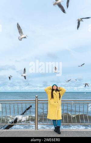 Sorglose Frau, die Spaß am Meer hat, mit Möwen, die in der Luft fliegen Stockfoto