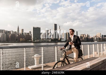 Geschäftsmann mit Kaffeetasse und Radfahren auf dem Fluss in New York City, USA Stockfoto