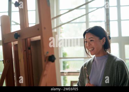 Glückliche Frau mit Pinsel, die Malerei in der Werkstatt bewundert Stockfoto
