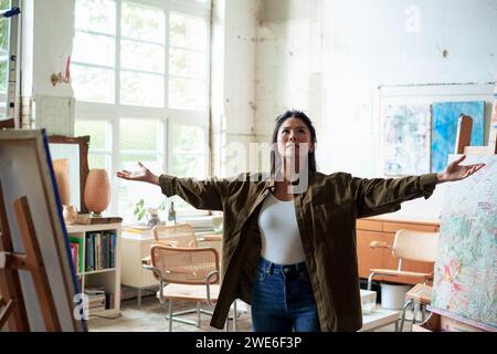 Selbstbewusster Maler, der mit ausgestreckten Armen im Kunststudio steht Stockfoto