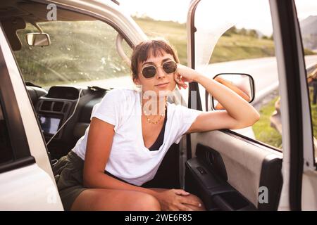 Lächelnde junge Frau, die sich an der Autotür lehnt Stockfoto
