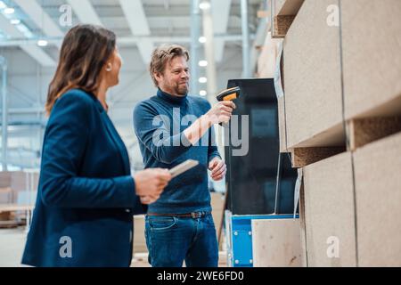 Lächelnder Geschäftsmann, der Barcode auf Holzdielen scannt, von einem Kollegen aus der Industrie Stockfoto