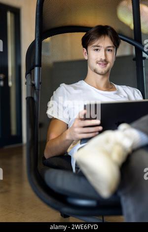 Junger Geschäftsmann mit Tablet-Computer, der auf Stuhl sitzt Stockfoto