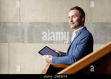 Durchdachter Geschäftsmann mit Tablet-PC an der Wand Stockfoto