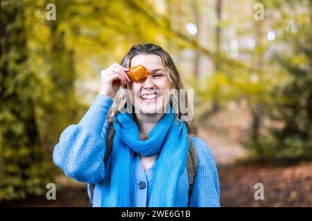 Glückliche junge Frau, die im Wald Blatt über dem Auge hält Stockfoto