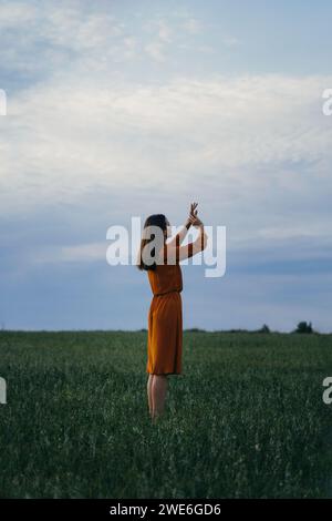 Frau mit erhobenen Händen und Gesten im Feld vor dem Himmel bei Sonnenuntergang Stockfoto