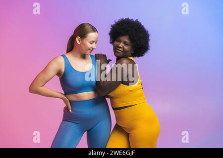 Lächelnde junge multirassische Freundinnen, die vor farbigem Hintergrund stehen Stockfoto