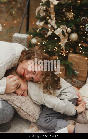 Lächelnde Mutter lehnt sich zu Hause an den Sohn in der Nähe des Weihnachtsbaums Stockfoto