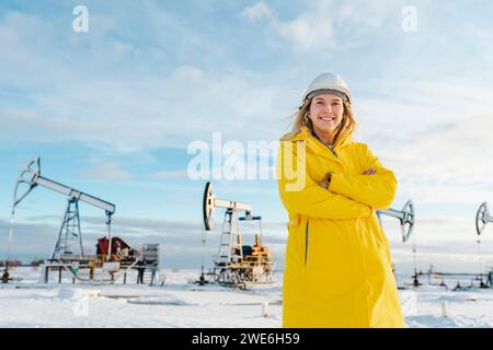 Lächelnder junger Ingenieur mit überkreuzten Armen, der im Winter auf dem Ölförderfeld stand Stockfoto