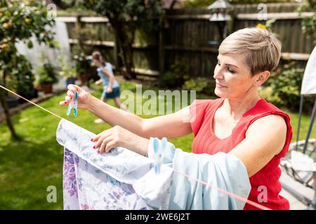 Mutter trocknet Wäscheseil mit Tochter, die im Garten spielt Stockfoto