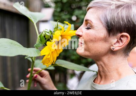 Lächelnde Frau, die Sonnenblume im Garten riecht Stockfoto