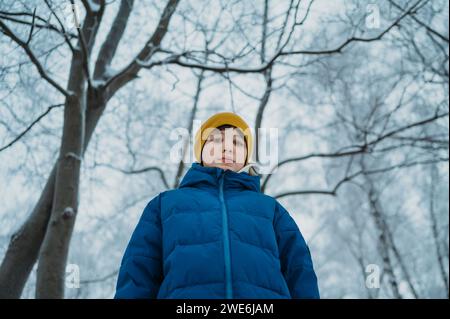 Junge mit Winterjacke in der Nähe von Bäumen im Wald Stockfoto
