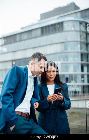 Geschäftsmann und Geschäftsfrau benutzen das Smartphone vor dem Gebäude Stockfoto