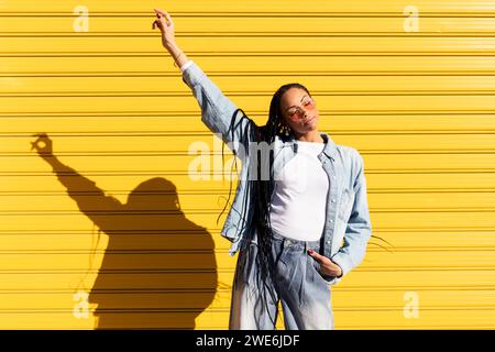 Frau mit erhobener Hand, die am sonnigen Tag vor einem Wellpappenverschluss steht Stockfoto