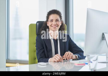 Glückliche, reife Geschäftsfrau, die mit Computer am Schreibtisch sitzt Stockfoto