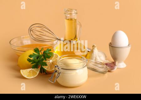 Glas mit frischer Mayonnaise und Zutaten auf beigefarbenem Hintergrund Stockfoto
