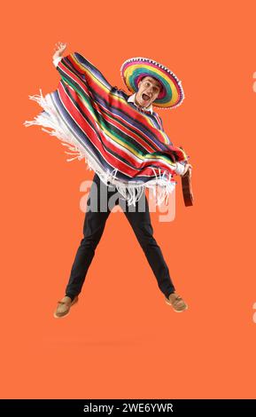 Mexikanischer junger Mann mit Sombrero-Hut, der auf orangefarbenem Hintergrund springt Stockfoto