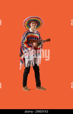 Mexikanischer junger Mann mit Sombrero-Hut, der Gitarre auf orangem Hintergrund spielt Stockfoto