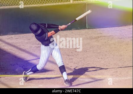 Ein Baseball-Softball-Spieler schwingt die Fledermaus und schlägt den Ball mit Flare Stockfoto