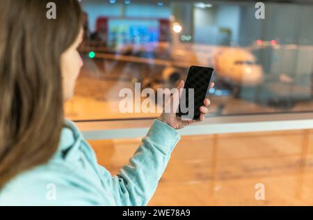 Das Mädchen hält ein Smartphone mit einem schwarzen Bildschirm in der Nahaufnahme. Telefon im Hintergrund des Flughafens mit einem Flugzeug. Telefon in der Hand und ein Flugzeug in der Badewanne Stockfoto