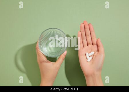 Ein Glas Wasser wird in der linken Hand gehalten und mehrere weiße Tabletten in der rechten Hand. Medikamenten- und Rezeptpillen-Konzept Stockfoto