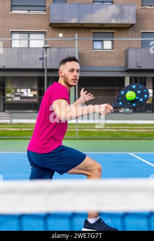 Porträt eines jungen Mannes, der während eines Spiels Rückhand-Pickleball schlägt Stockfoto