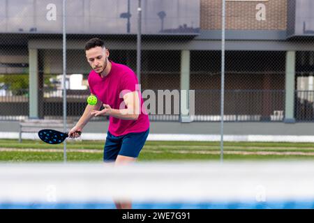 Porträt eines Mannes, der eine Portion im Pickleball vorführt. Sportlicher Spieler mit Pickleball trainiert auf dem Freiplatz mit einem Schläger, um den Ball zu schlagen Stockfoto