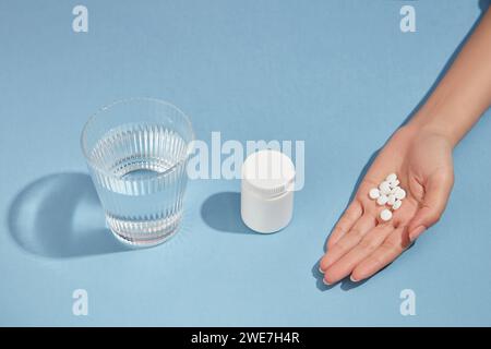 Ein Glas Wasser, eine unbeschriftete Arzneimittelflasche und eine Handvoll Pillen sind in einer Zeile auf blauem Hintergrund angeordnet. Medizin, Behandlungen und Gesundheitswesen Stockfoto