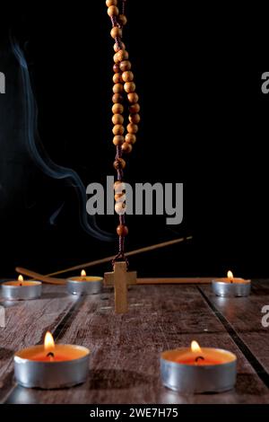 Kreis aus beleuchteten Kerzen mit einem hölzernen Rosenkranz betenden Perlen in der Mitte und einem schwelenden Weihrauch im Hintergrund isoliert auf schwarzem Hintergrund Stockfoto