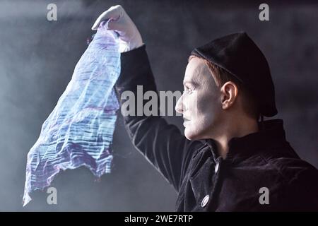 Dramatisches Seitenporträt eines Mime-Künstlers, der auf der Bühne auftritt und das schimmernde Tuch am Licht hält, Kopierraum Stockfoto