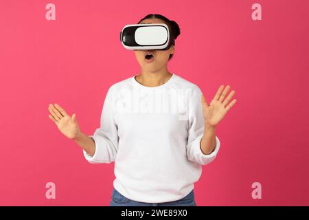 Überraschte junge asiatische Frau, die ein Virtual-Reality-Headset trägt und vor Aufregung gespendet ist Stockfoto