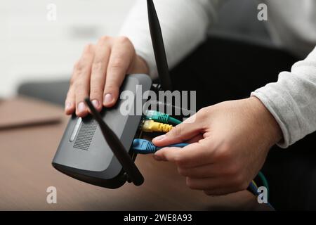 Mann, der Kabel in den WLAN-Router an einem Holztisch drinnen steckt, Nahaufnahme Stockfoto