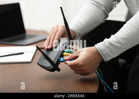 Mann, der Kabel in den WLAN-Router an einem Holztisch drinnen steckt, Nahaufnahme Stockfoto