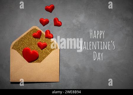 Postkarte, Umschlag mit rotem Herz innen, auf grauem Betonhintergrund, mit Text Happy Valentinstag, Draufsicht, Liebe, Valentinstag 14. Februar Stockfoto