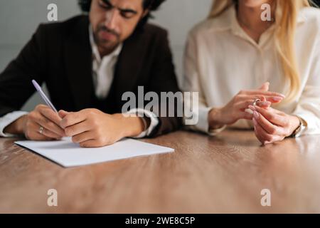 Abgeschnittene Aufnahme von Ehepaaren, die Dekretpapiere unterzeichnen und sich im Anwaltsbüro am Schreibtisch scheiden lassen. Unglückliche Trennung der verheirateten Familie Ende Stockfoto