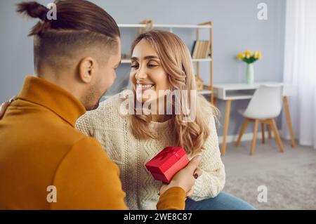Glückliches, schönes, liebevolles, junges Paar zu Hause in romantischer Atmosphäre feiern Valentinstag, Mann gratuliert der Frau, schenkt Geschenke. Stockfoto