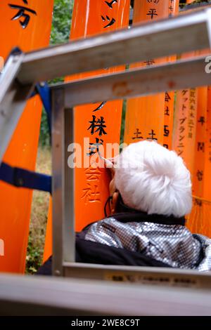 Ein Ältester malte sorgfältig die leuchtenden orangen Torii-Tore am Fushimi Inari-Schrein in Japan Stockfoto