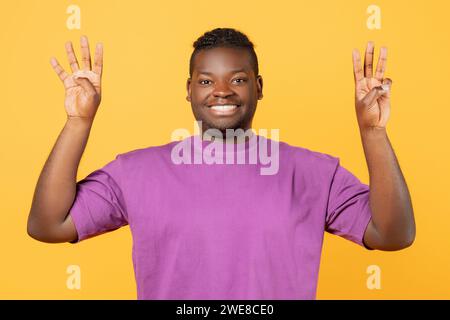 Der schwarze Kerl hebt die Hände und zeigt die Nummer sieben vor gelbem Hintergrund Stockfoto