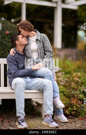 Herbstromane: Ein junges Paar umarmen und küssen auf der Park Bank. Ein junges Paar küsst und freut sich am See. Schönes junges Paar, das sich draußen küsst Stockfoto