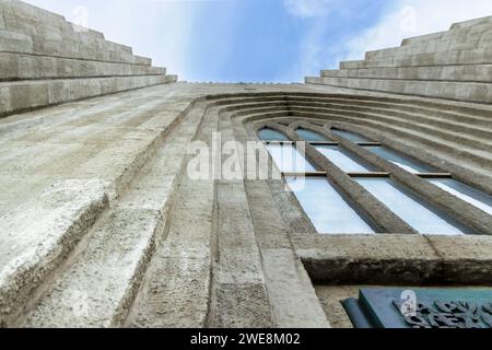 Von unten außen ist eine alte Stufenbeton-Fassade mit bogenförmigen Glasfenstern und eine Gedenktafel mit Worten am Eingang der Pfarrkirche Hallgrimskirkja Stockfoto