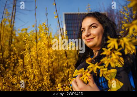 Junge glückliche lächelnde Frau plus Größe im Frühling im Stadtpark zwischen blühenden gelben Forsythienbüschen Stockfoto