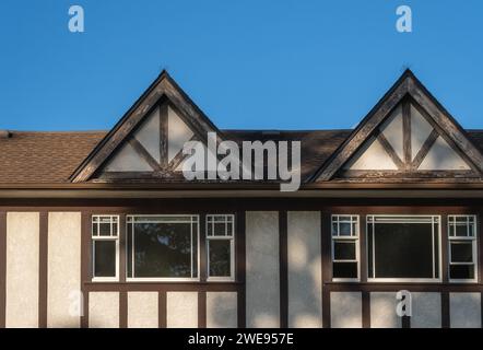 Das Dach des Hauses mit schönen Fenstern. Häuser mit Schindeldach gegen blauem Himmel. Kante der Dachschindeln oben auf den Häusern dunkle Asphaltziegel auf t Stockfoto