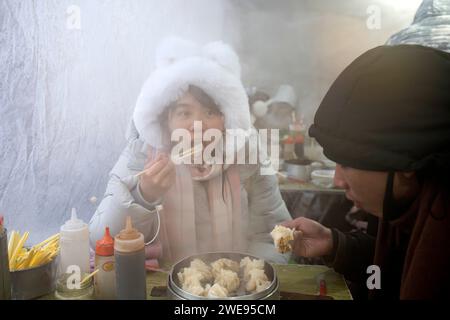 Harbin, Chinas Provinz Heilongjiang. Januar 2024. Touristen essen „Shaomai“, ein traditionelles gedämpftes Gebäck auf dem Hongzhuan Morning Market in Harbin, nordöstlich Chinas Provinz Heilongjiang, 22. Januar 2024. Harbin's Morning Markets, bekannt für ihr vielfältiges Angebot zu vernünftigen Preisen, waren ein beliebter Treffpunkt für Touristen. Der Morning Market in der Hongzhuan Street war einer der ersten lokalen Morning Markts, der in letzter Zeit berühmt wurde. An den Imbissständen, die dampfende lokale Frühstücksgerichte servieren, wimmelt es von Touristen, die gerne lokale Köstlichkeiten probieren möchten. Quelle: Cai Yang/Xinhua/Alamy Live News Stockfoto