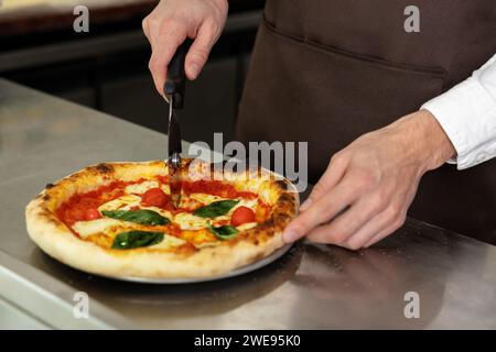 Nahaufnahme von Manns Händen, die Pizza schneiden Stockfoto